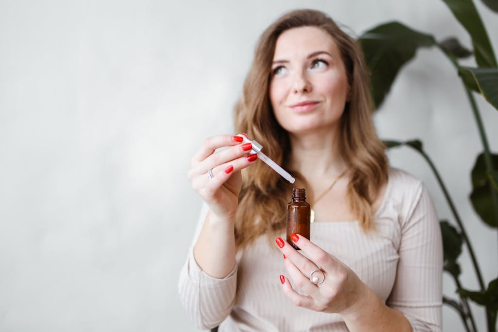 A woman holds a brown bottle and dropper indoors, surrounded by green plants.