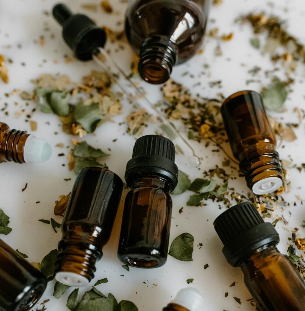 Brown glass bottles of essential oils surrounded by dried herbs on a white surface.