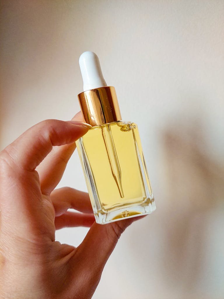 Close-up of a hand holding a glass dropper bottle with golden serum, ideal for beauty and skincare themes.
