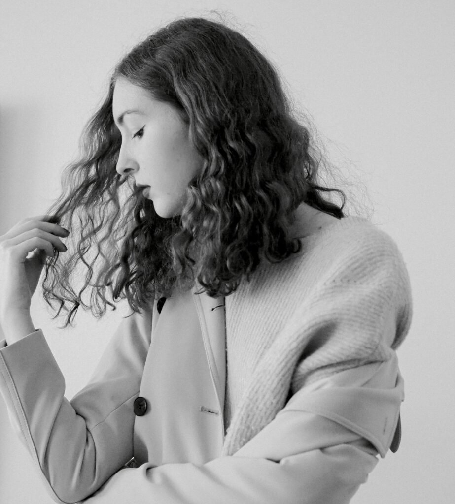 Black and white portrait of a woman in fashion coat and sweater posing in studio.