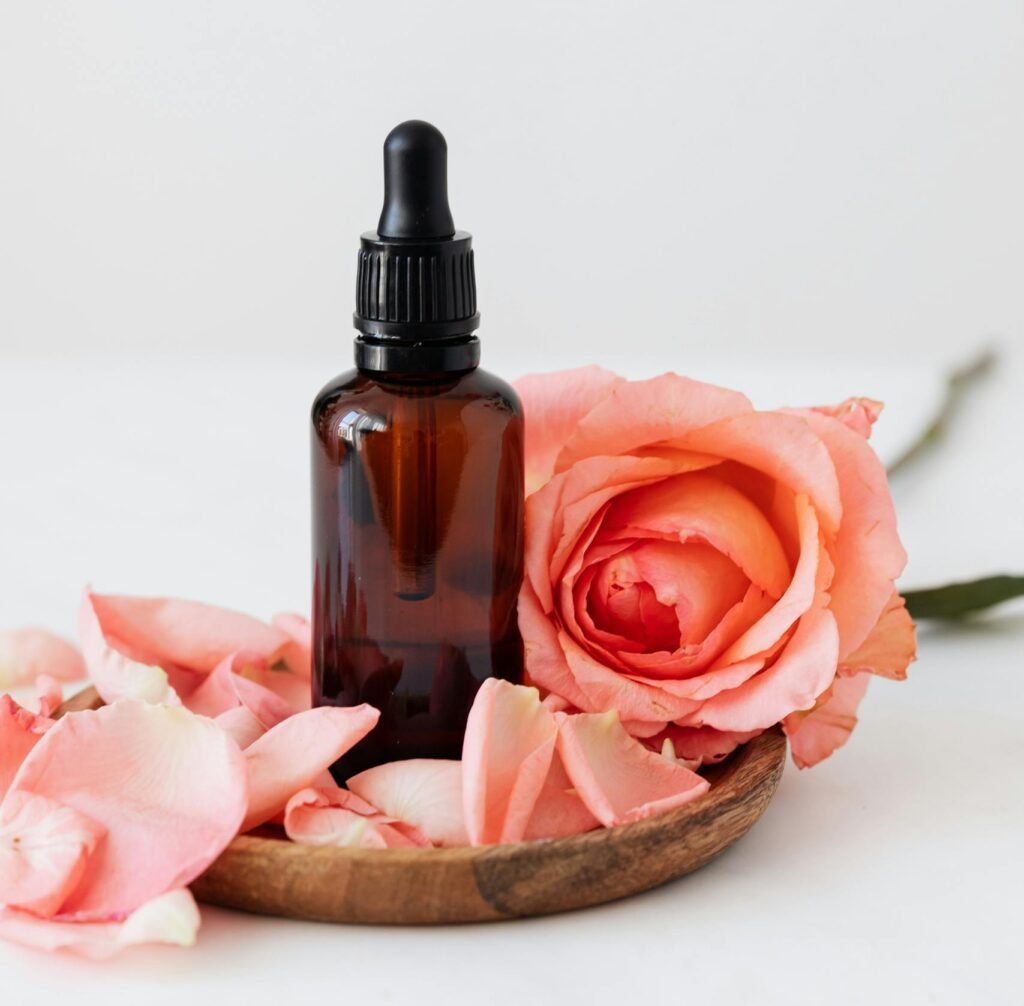 Elegant dropper bottle with pink rose petals on a wooden plate, perfect for aromatherapy or skincare.