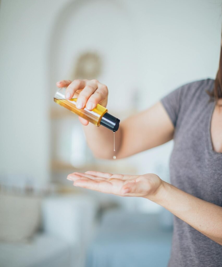 Close-up of a woman pouring massage oil into her hand in a serene spa setting, promoting relaxation.