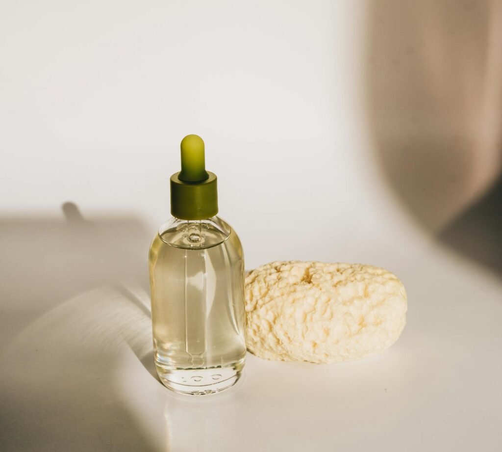 Glass bottle of skincare oil with dropper and natural sponge on a minimalistic setup.