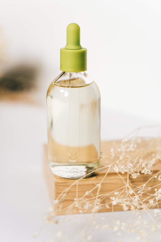 A clear glass dropper bottle with liquid on a wooden board, adorned with delicate dried flowers.