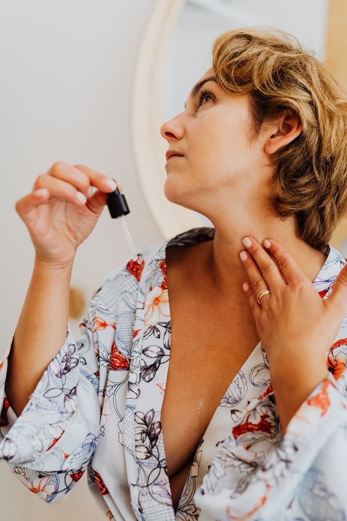 Woman in a floral robe applying skincare serum with a dropper indoors.