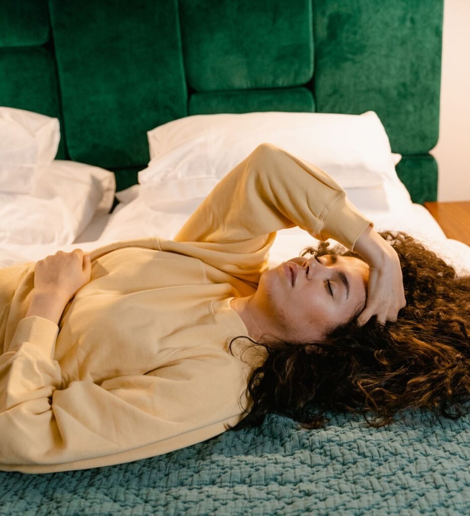 Young woman relaxes on a bed with hand on forehead, depicting fatigue or headache.