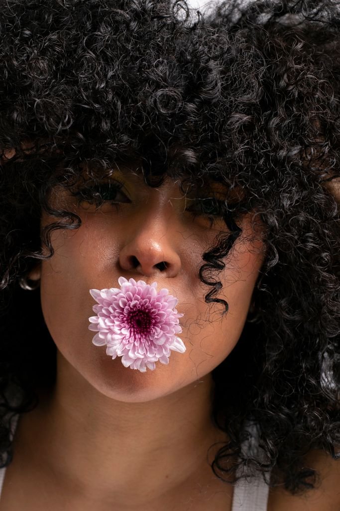 A striking portrait of a person with curly hair and a flower in their mouth.